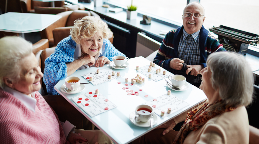Group of Older Adults Sitting at Table, Talking and Playing Bingo