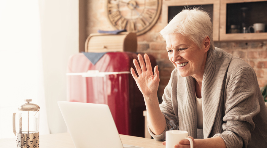Older Woman Making Video Call on Laptop in Kitchen, Waving at the Screen