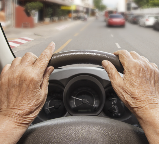 Older Woman's Hands on Car Steering Wheel, Driving on a City Street