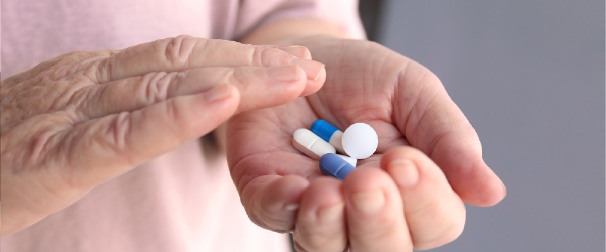 Older Adult's Hands Holding White and Blue Medication