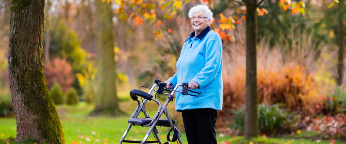 Older Adult Woman with Walker in Front of Nature Park with Orange Leaves